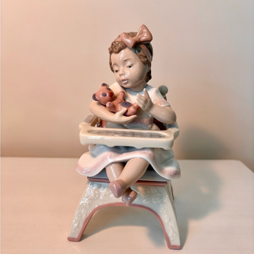 Lladro Porcelain Figurine of Girl with Teddy Bear sitting in a high chair.